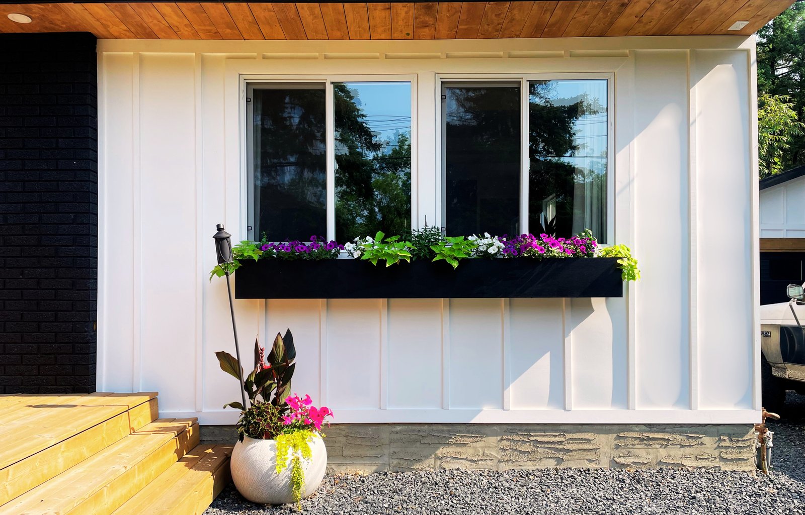 modern black window box full of plants on house with white board and batten siding and wood accents